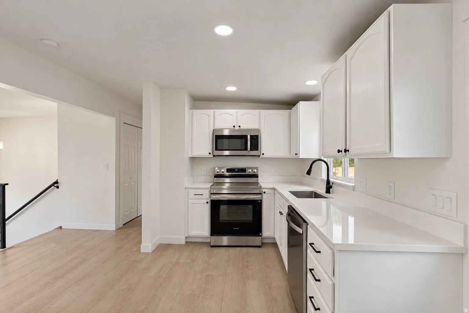 Contemporary kitchen featuring white cabinetry, stainless steel appliances, light-toned wood-finish flooring, a matte black faucet, and recessed lighting