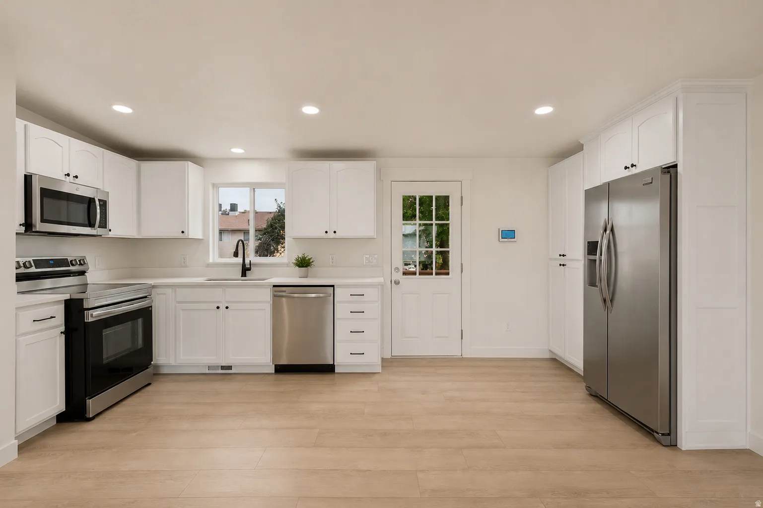 Full kitchen featuring white cabinetry, stainless steel appliances, wood-finish flooring, recessed lighting, and a paneled exterior door