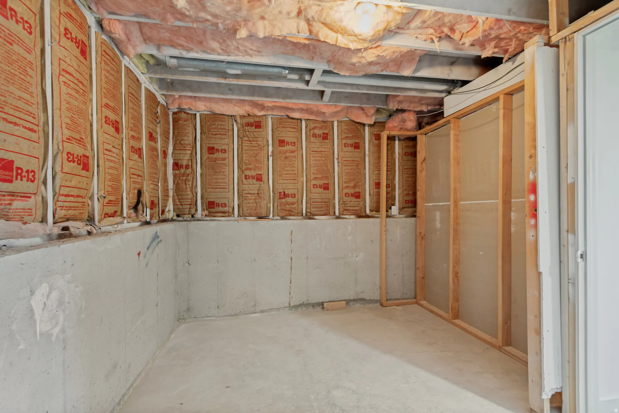 Unfinished interior space with exposed framing and insulation, concrete walls, and a concrete floor
