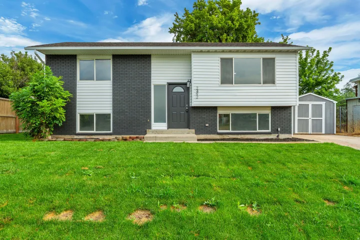 Split-level residence featuring brick and siding exterior, front lawn, concrete entry steps, and a detached storage shed