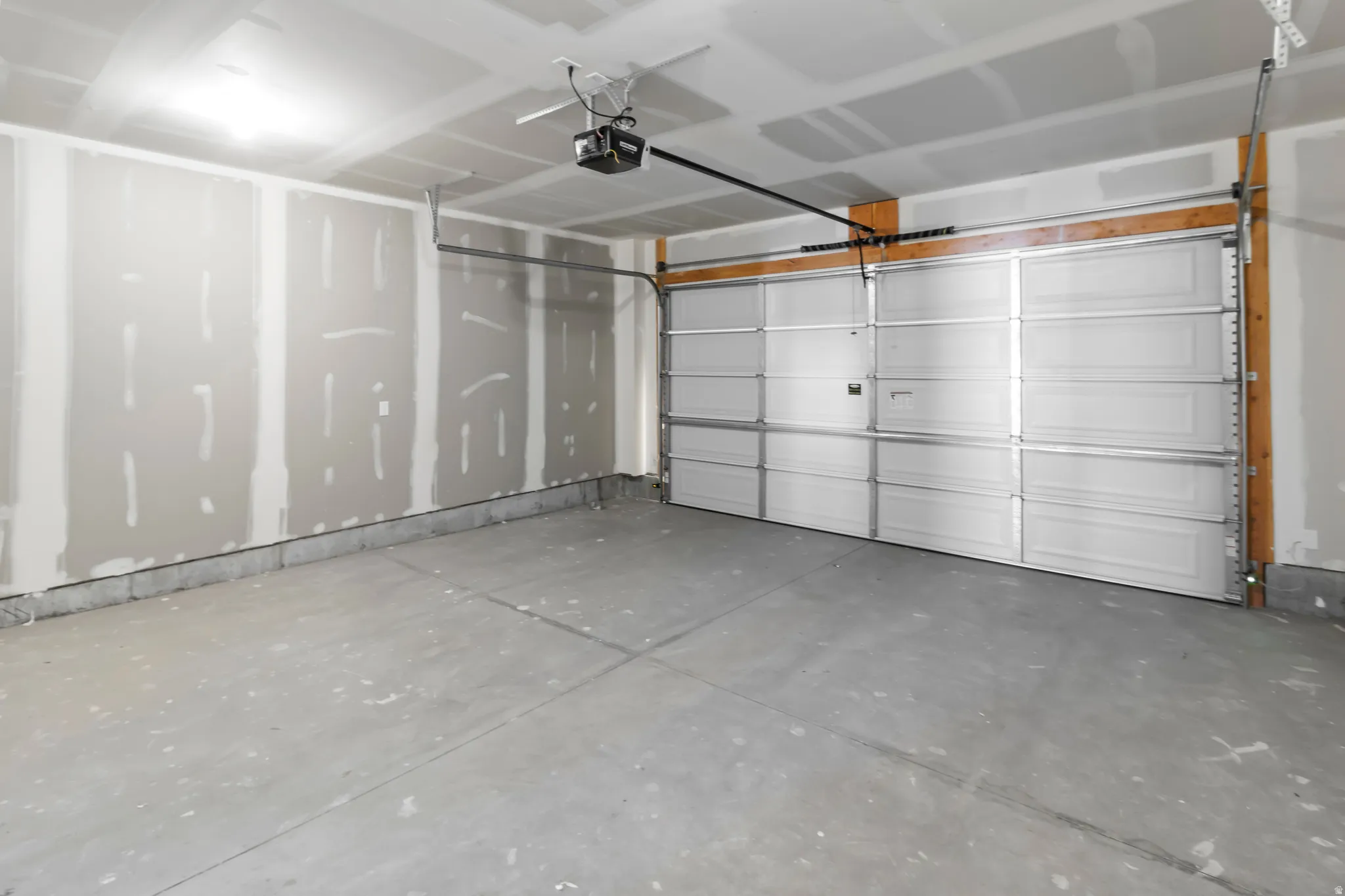 Attached two-car garage featuring a sectional overhead door, automatic opener, drywall walls, and a concrete floor