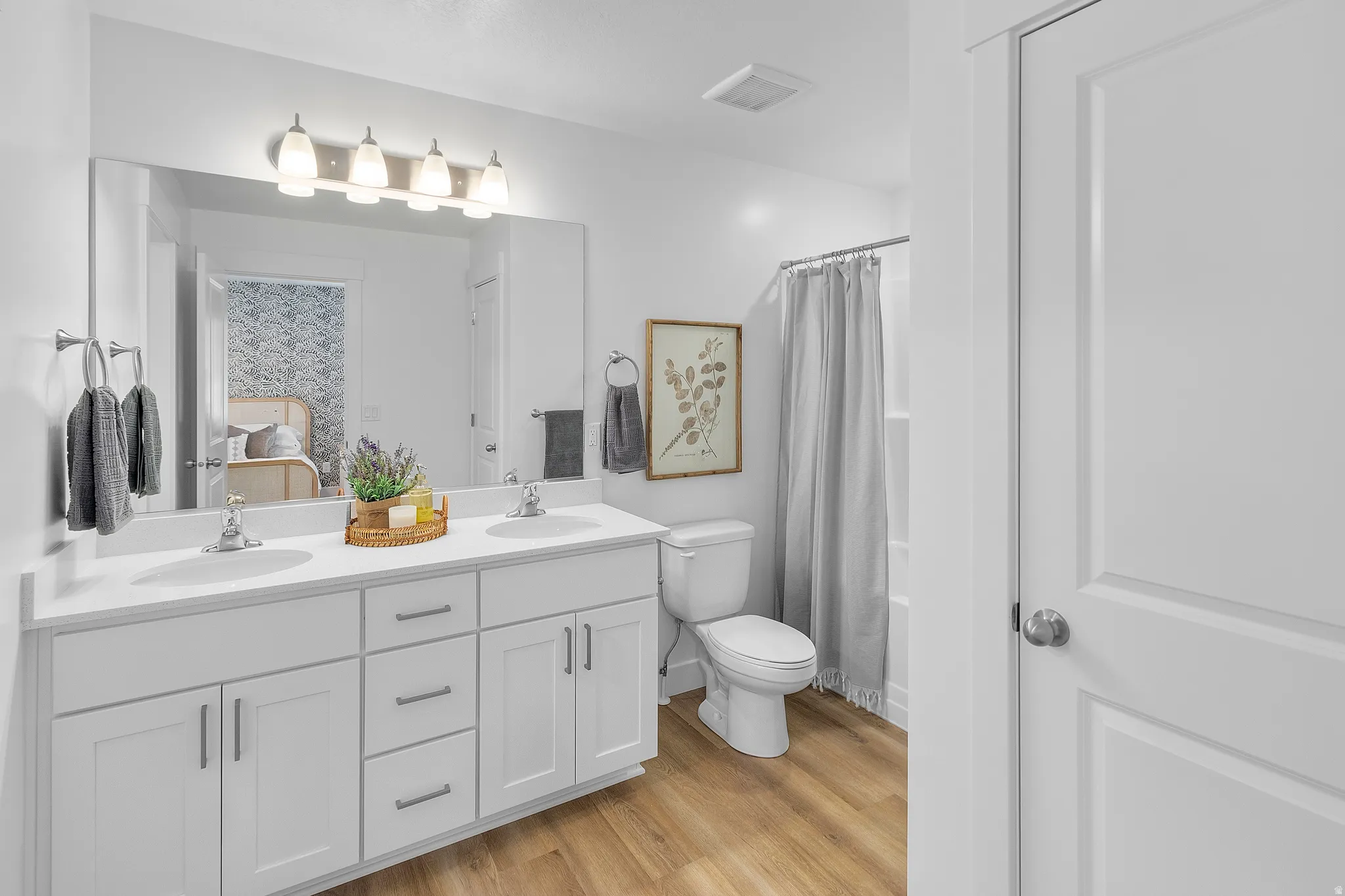 Double vanity with white cabinetry, wood-finish flooring, full-width mirror, and a shower with tub
