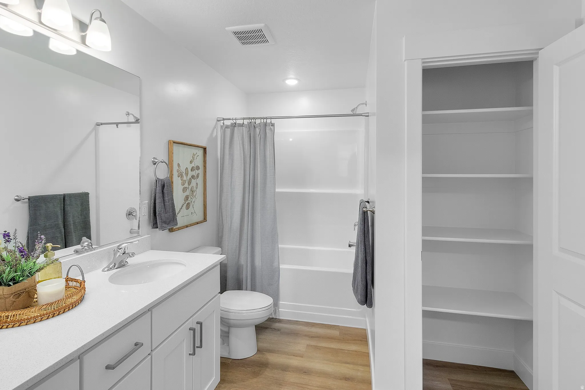 Bathroom featuring a white vanity with integrated sink, chrome faucet, white bathtub/shower combination, and wood-finish flooring