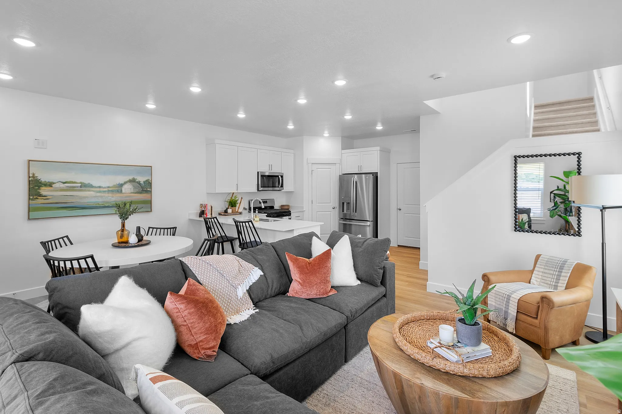Open-concept living space featuring wood-finish flooring, recessed lighting, and a white kitchen with stainless steel appliances