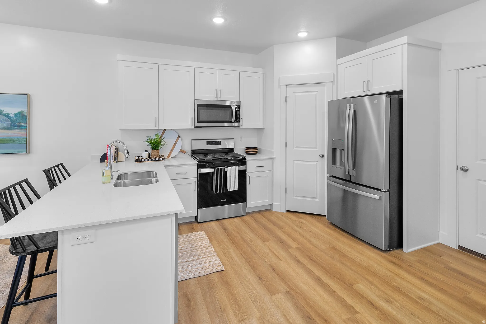 Kitchen featuring white cabinetry, stainless steel appliances, a kitchen island with an integrated sink, white countertops, and wood-finish flooring