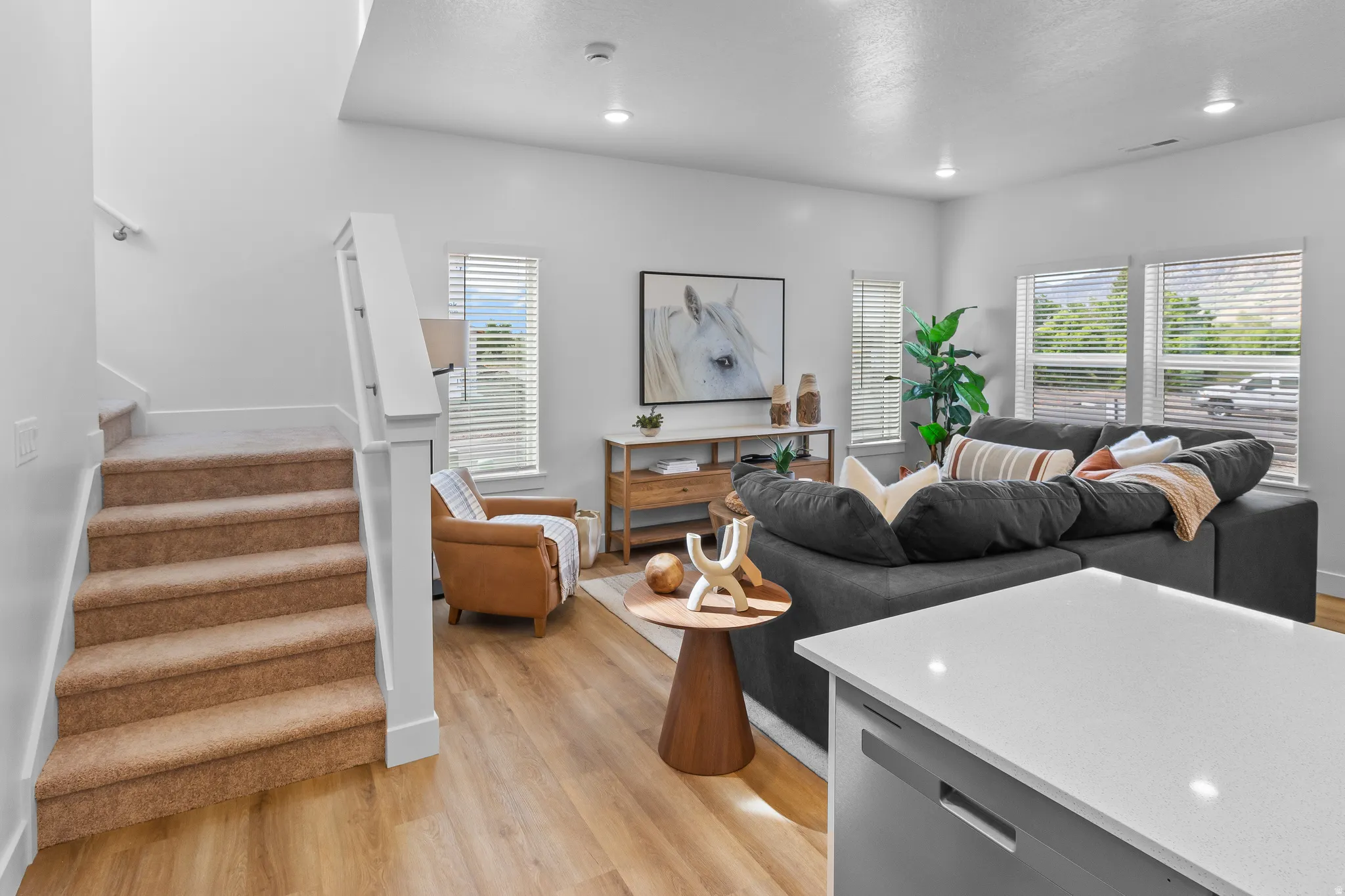 Wood-finish flooring throughout the main living area, white walls, recessed lighting, and a white kitchen island