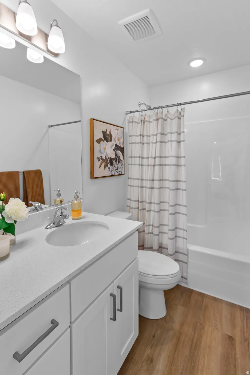 White vanity with a solid surface countertop, undermount sink, chrome faucet, and wood-finish flooring