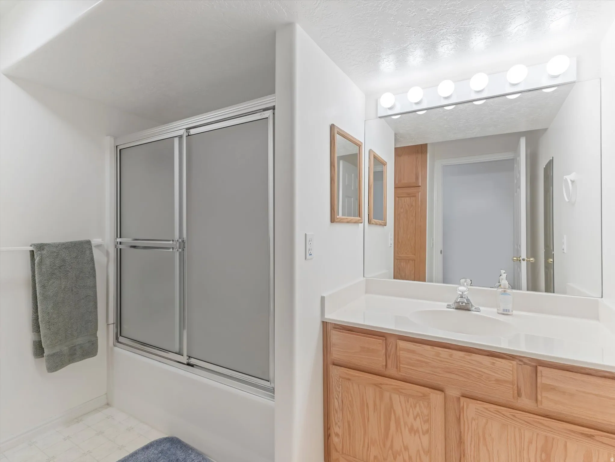Vanity with light wood-finish cabinetry, white countertop with integrated sink, and large mirror with strip lighting