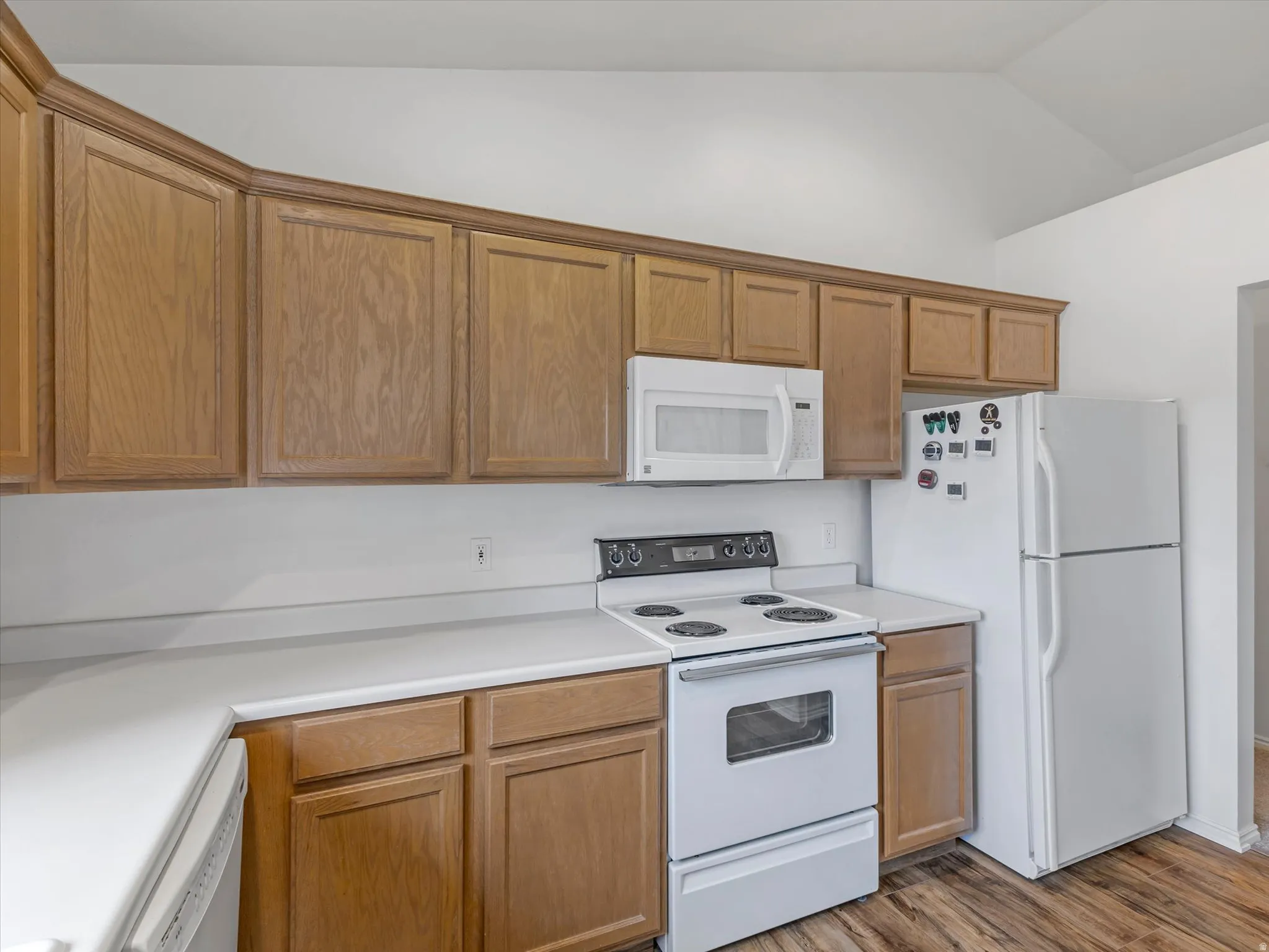 Wood-finish cabinetry, white countertops, built-in microwave, white electric range, and white refrigerator