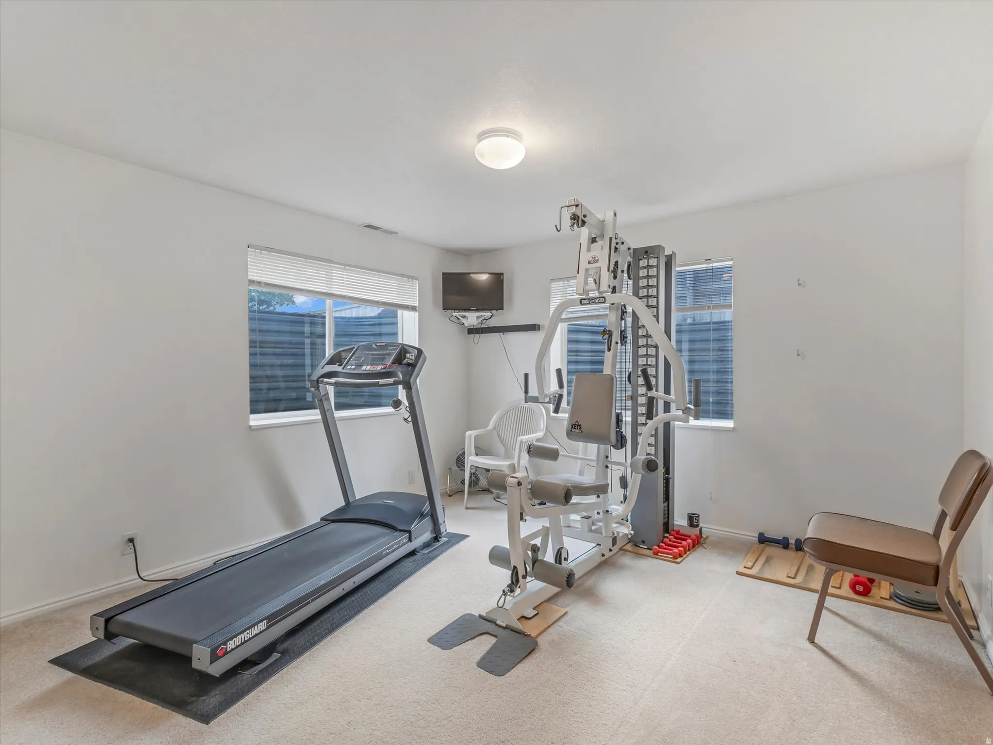 Recessed ceiling light, two windows with blinds, wall-mounted television bracket, and light-colored carpeting