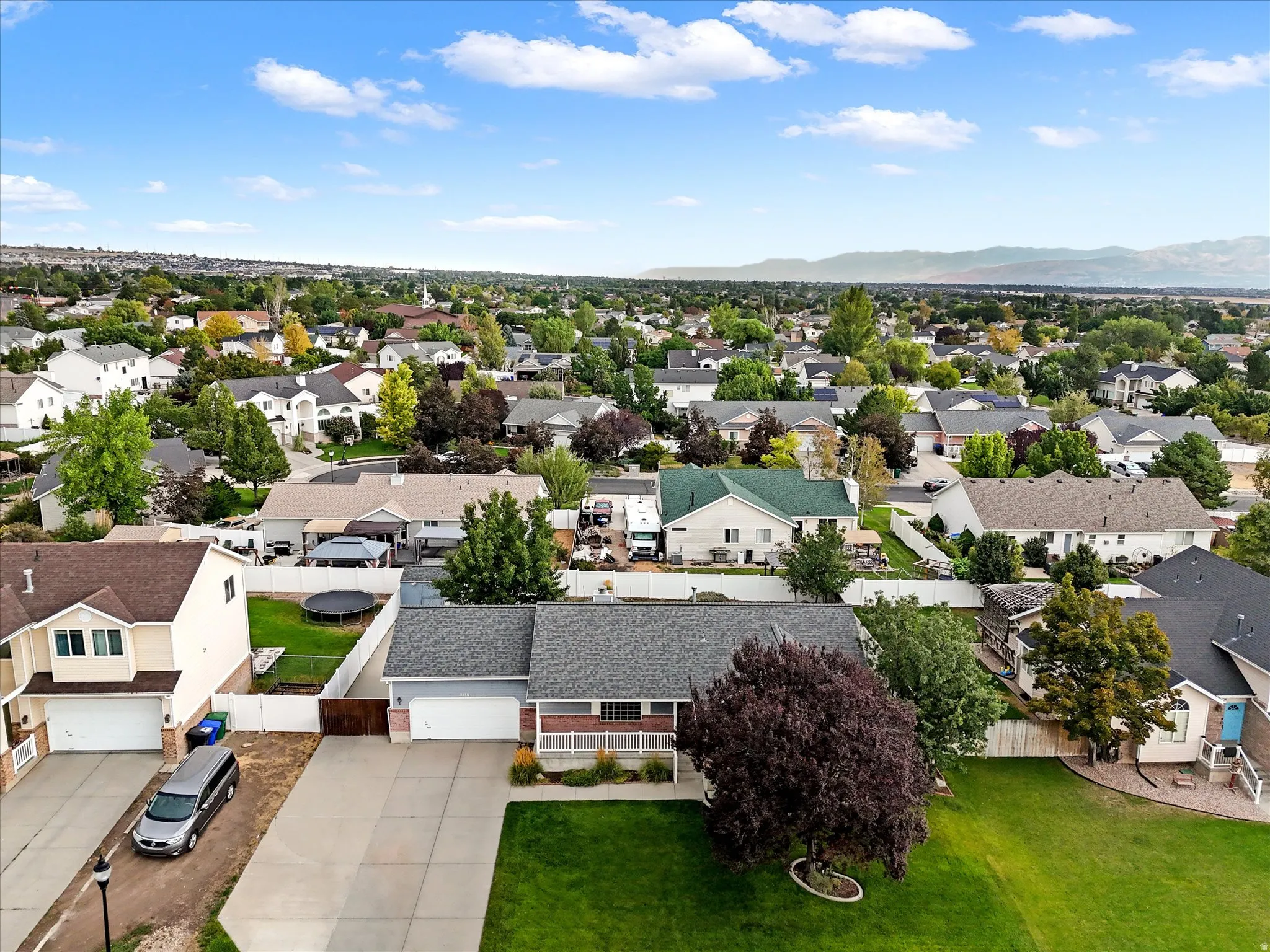 Aerial perspective showcasing a residential neighborhood with diverse housing styles, mature trees, and mountainous terrain in the background