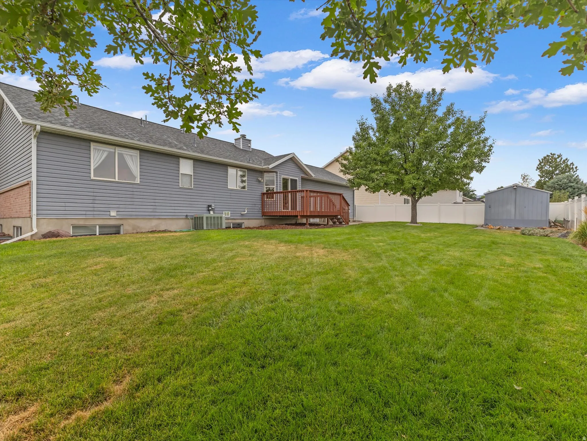 Expansive backyard featuring a manicured lawn, a large tree, a privacy fence, and a storage shed