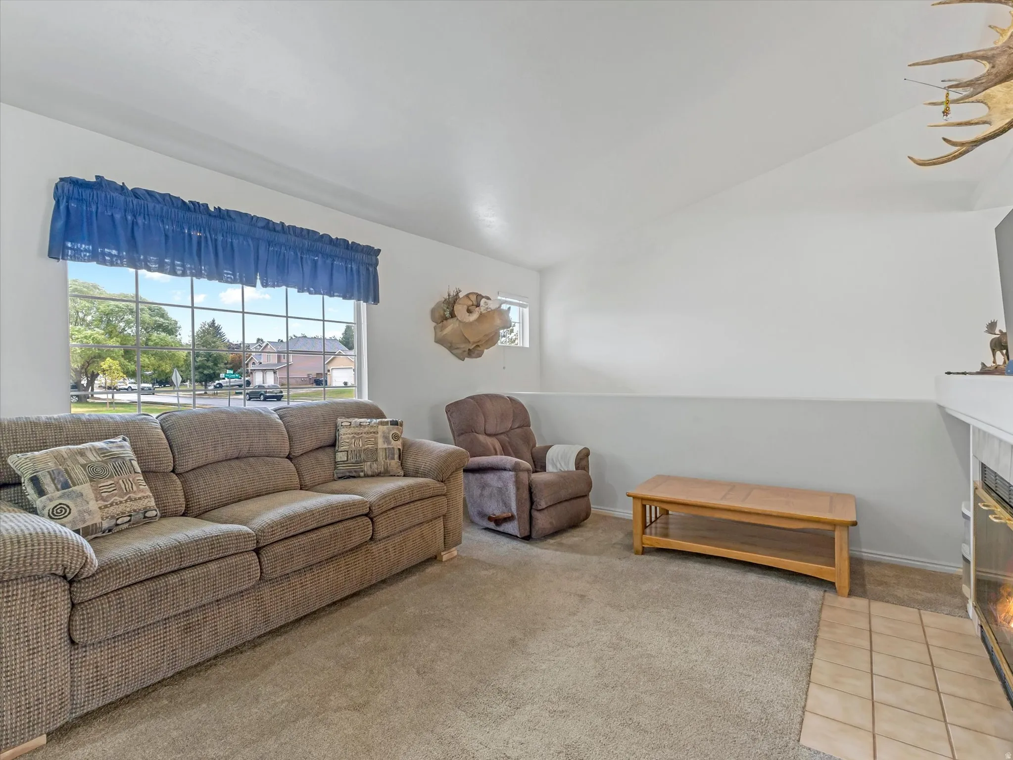 Bright living area featuring a large picture window, vaulted ceiling, and a fireplace with a tile hearth
