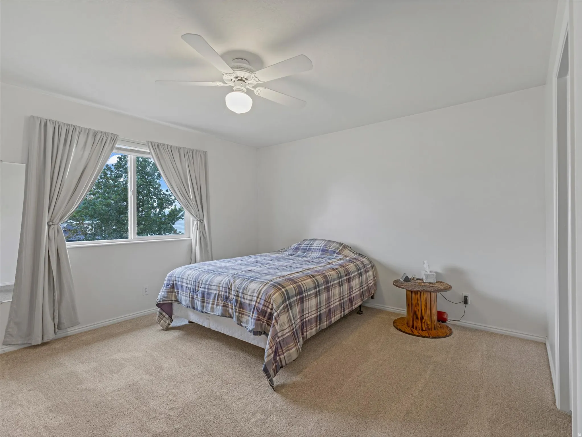 White ceiling fan with integrated lighting, window with white trim, light-colored carpeting, and light-colored walls