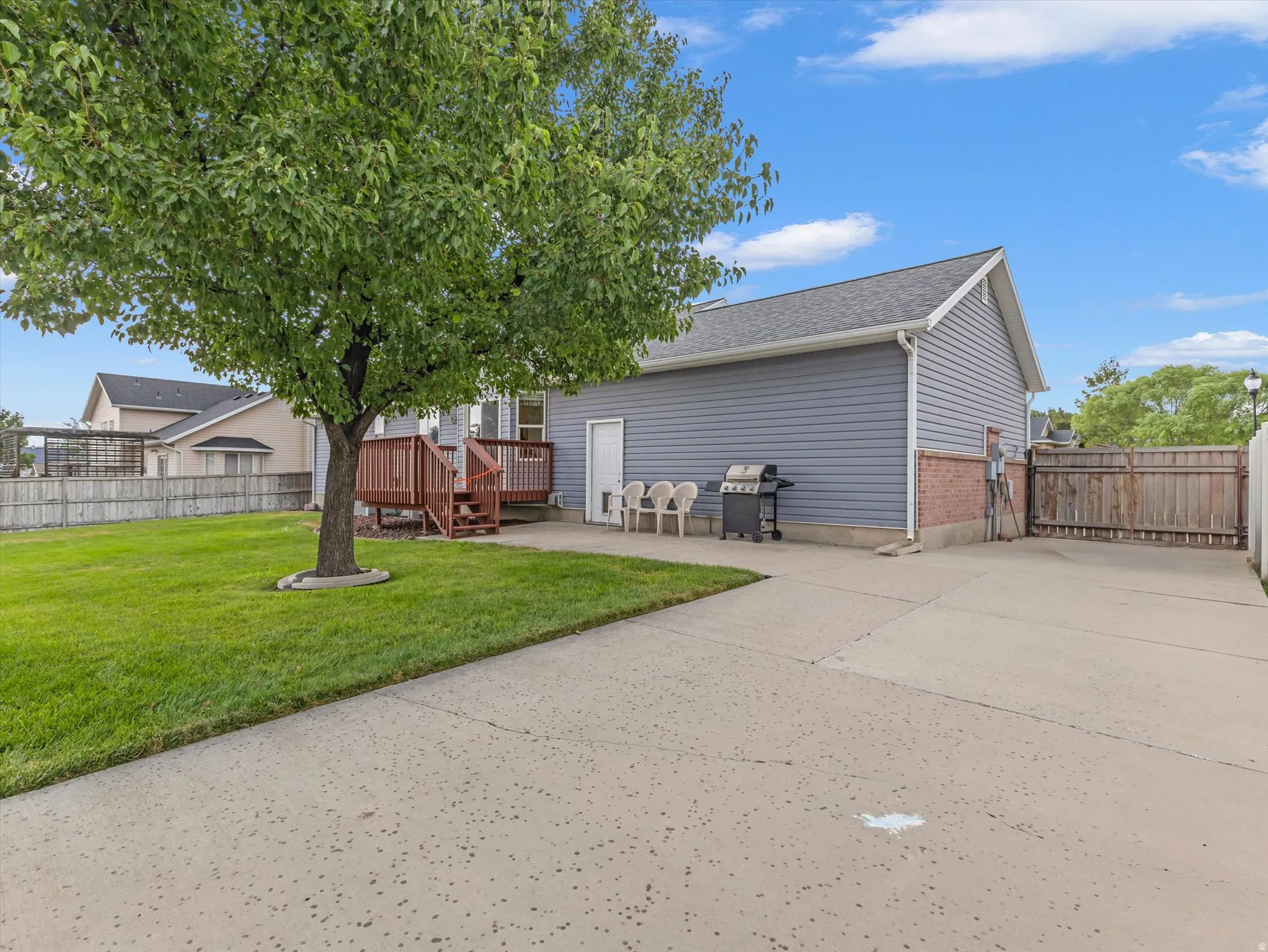 Expansive concrete patio with a wooden deck, mature tree, and fencing