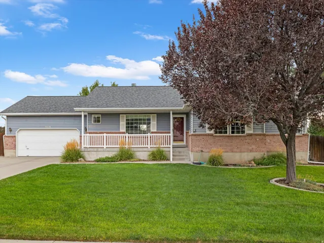 Siding exterior with brick accents, attached garage, covered front porch with white railing, and a manicured lawn