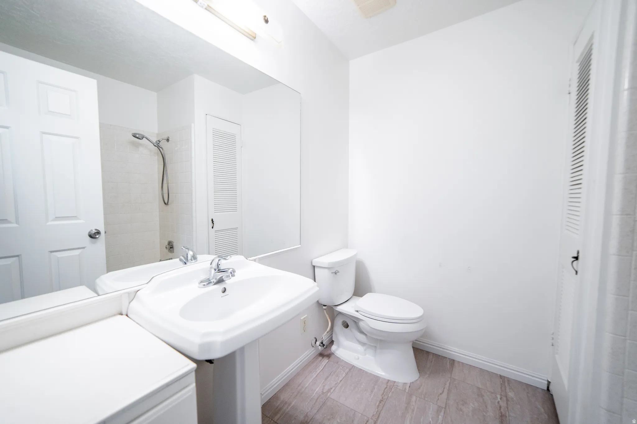 Pedestal sink with chrome fixtures, large wall-mounted mirror, white ceramic toilet, and light-toned wood-finish flooring