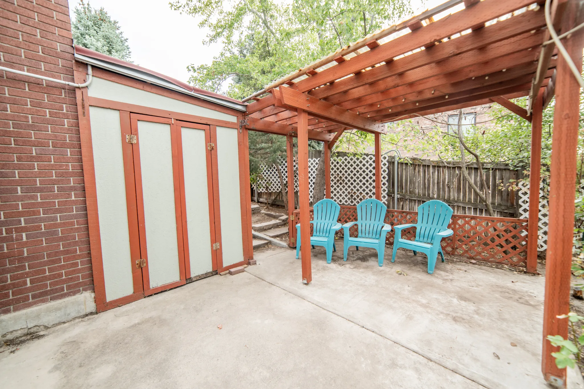 Red brick exterior, concrete patio, wood pergola, built-in storage unit, lattice fencing