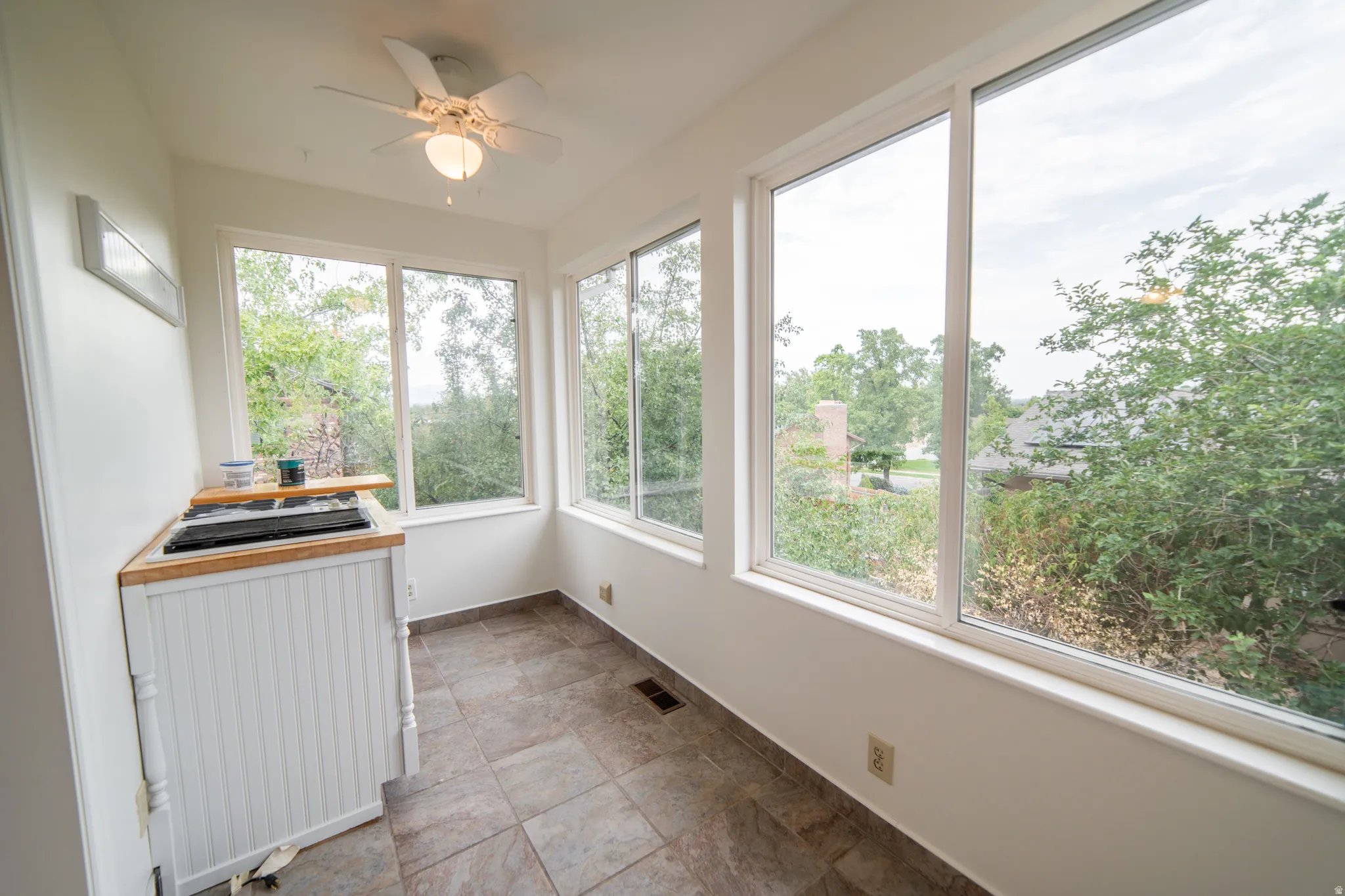 Sunroom with multiple large windows, a ceiling fan, tile flooring, and utility sink.