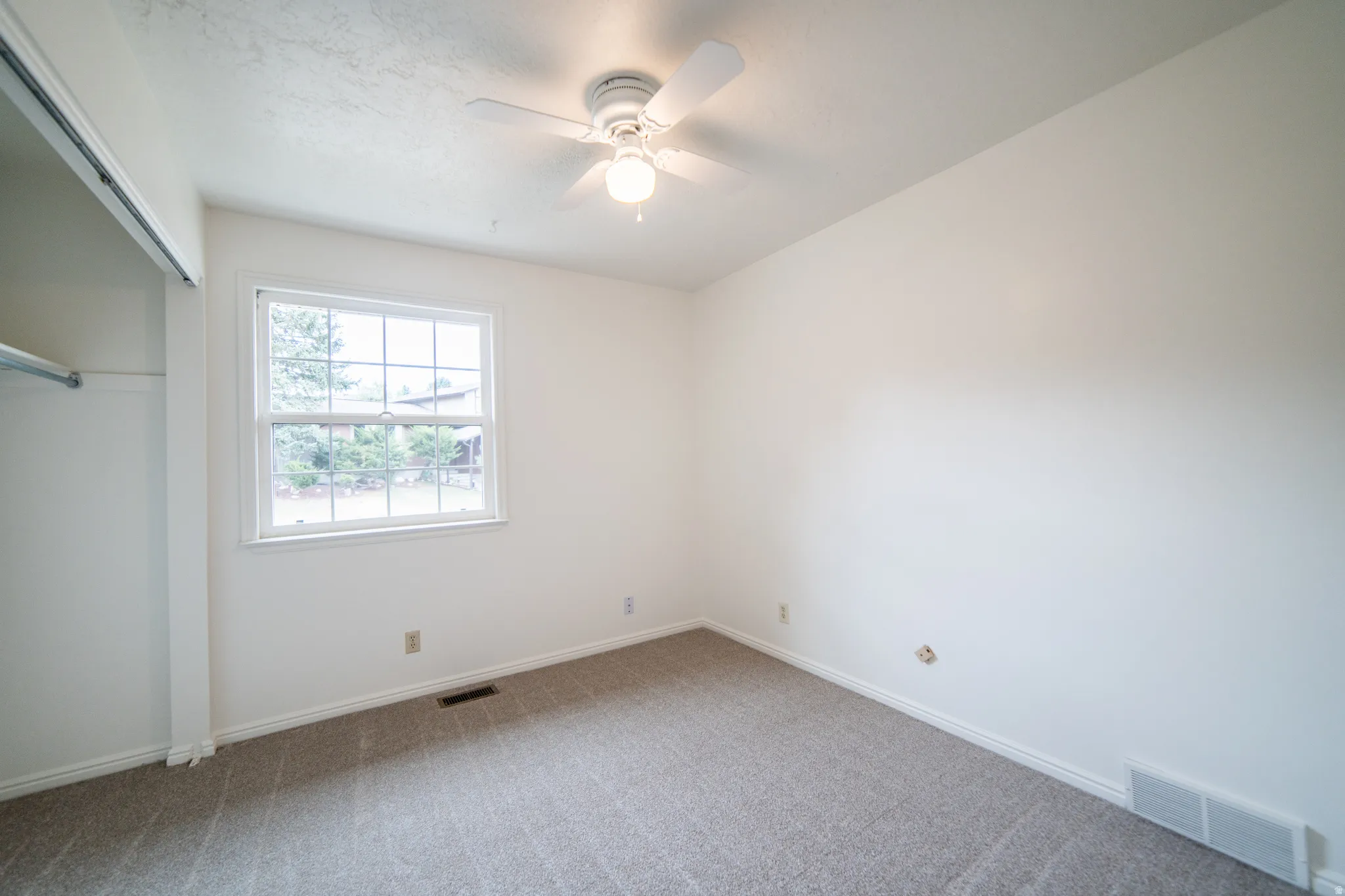 Room featuring neutral-toned carpet, a window with exterior visibility, and a ceiling fan with integrated lighting