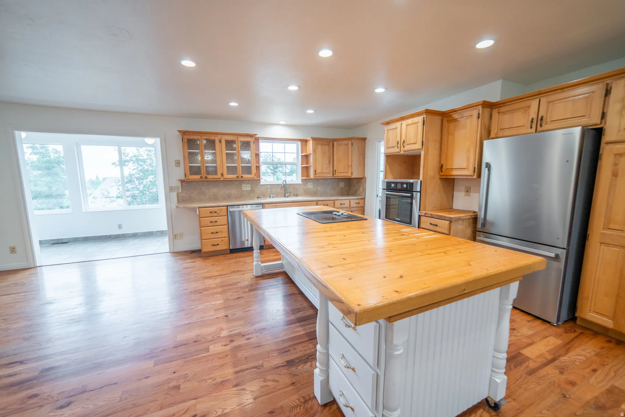 Kitchen featuring wood-finish flooring, recessed lighting, wood cabinetry, a built-in oven, and a stainless steel refrigerator