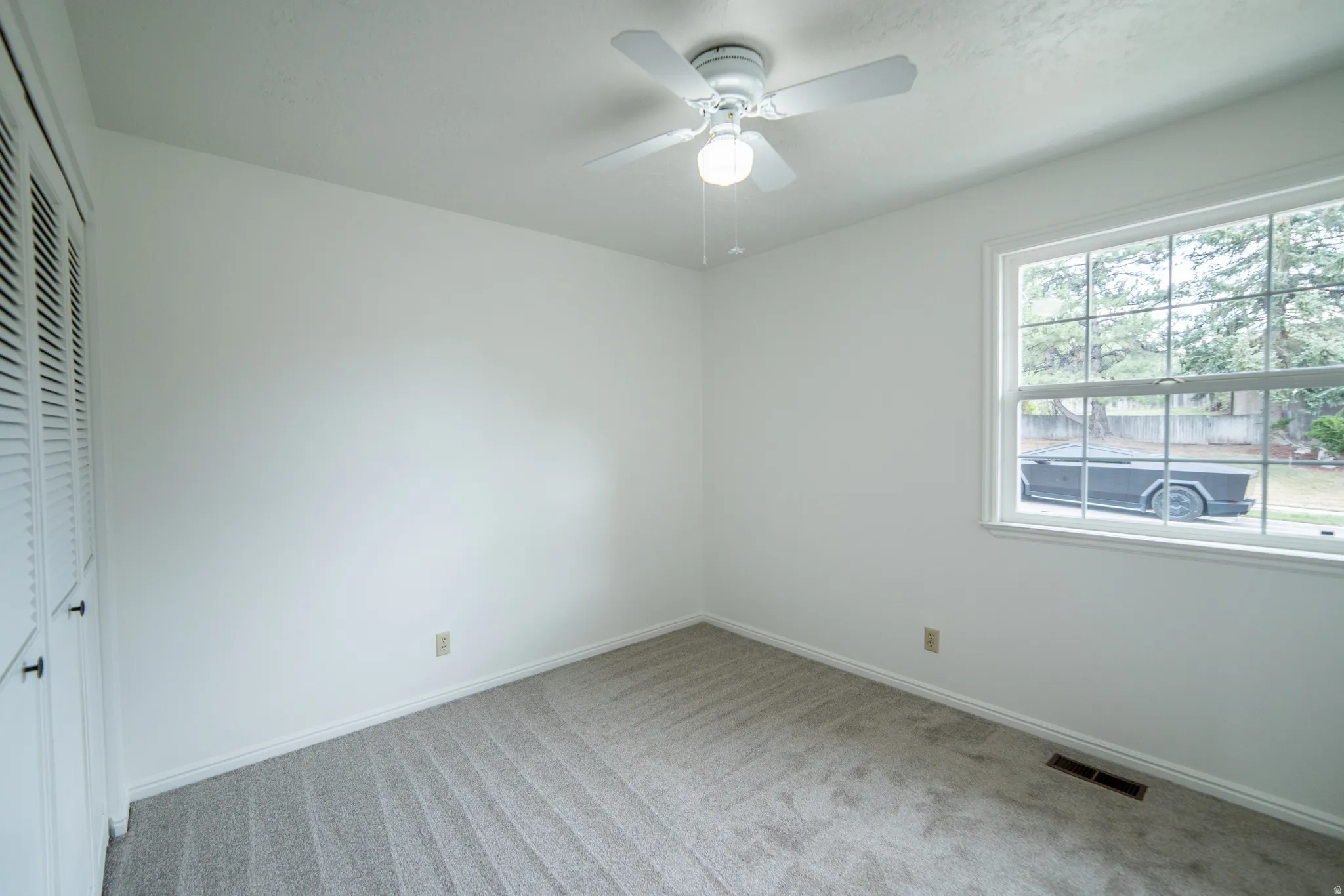 Carpeted flooring, white walls, louvered closet doors, and a ceiling fan with integrated lighting