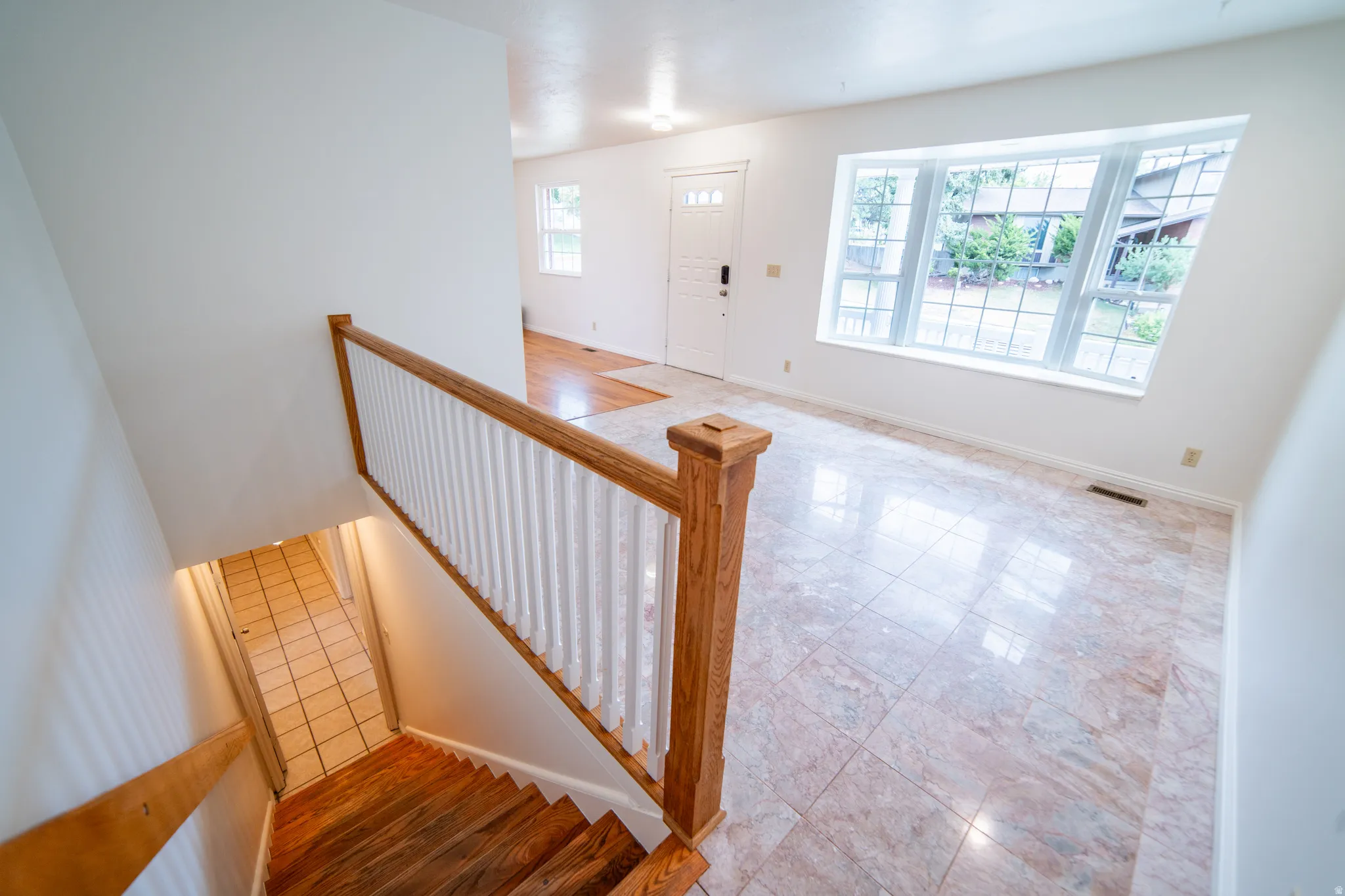 Bay window with gridded panes, tile flooring, wood-finish flooring, white painted walls, and a wooden staircase