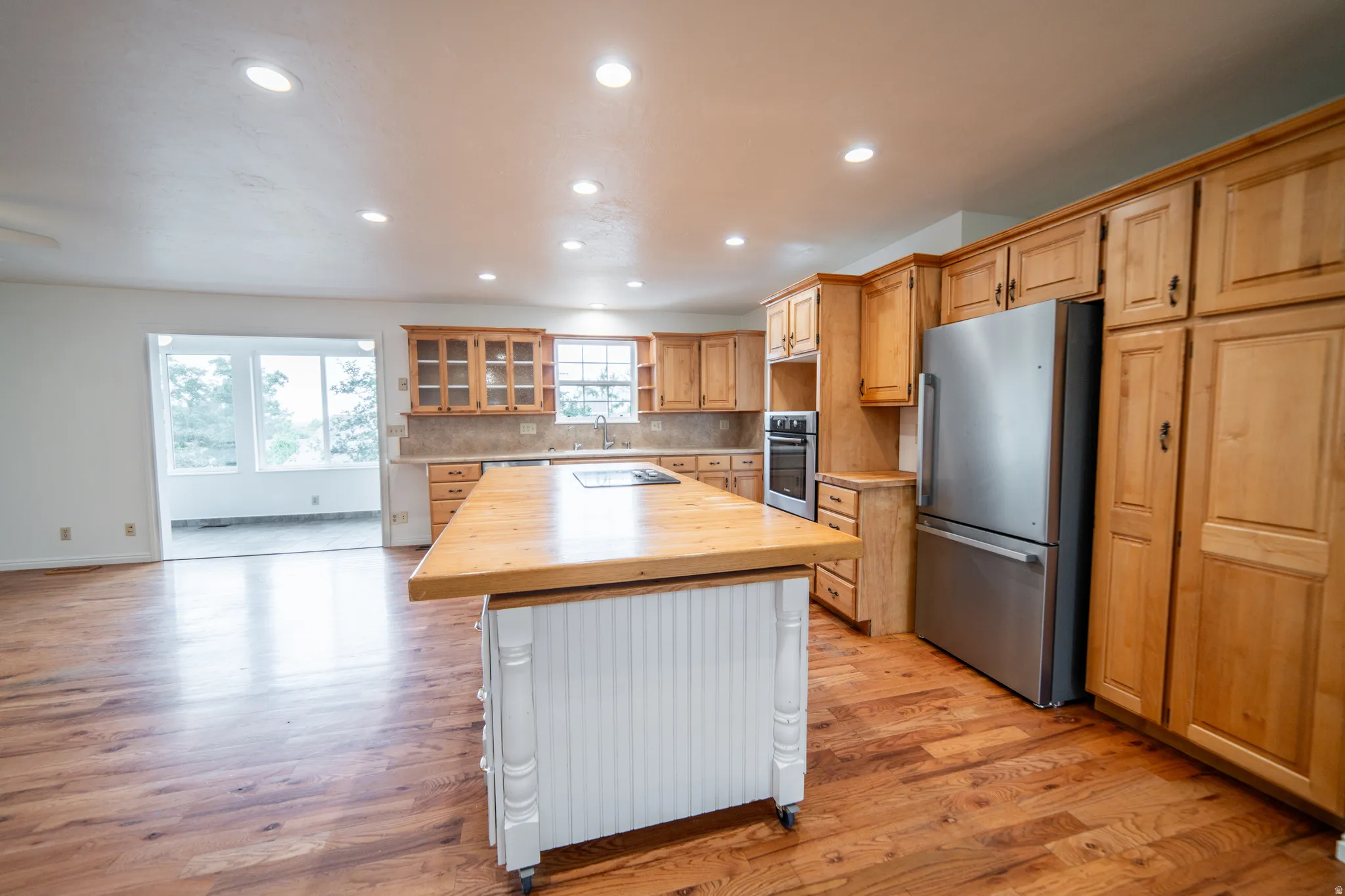 Spacious kitchen featuring wood-finish flooring, light wood cabinetry, stainless steel appliances, and a central island with a beautiful wood-finish countertop