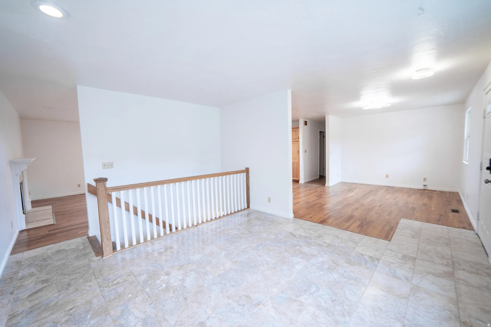 Bright interior with recessed lighting, tile flooring, wood-finish flooring, with white spindle on the banister guarding the stairs.