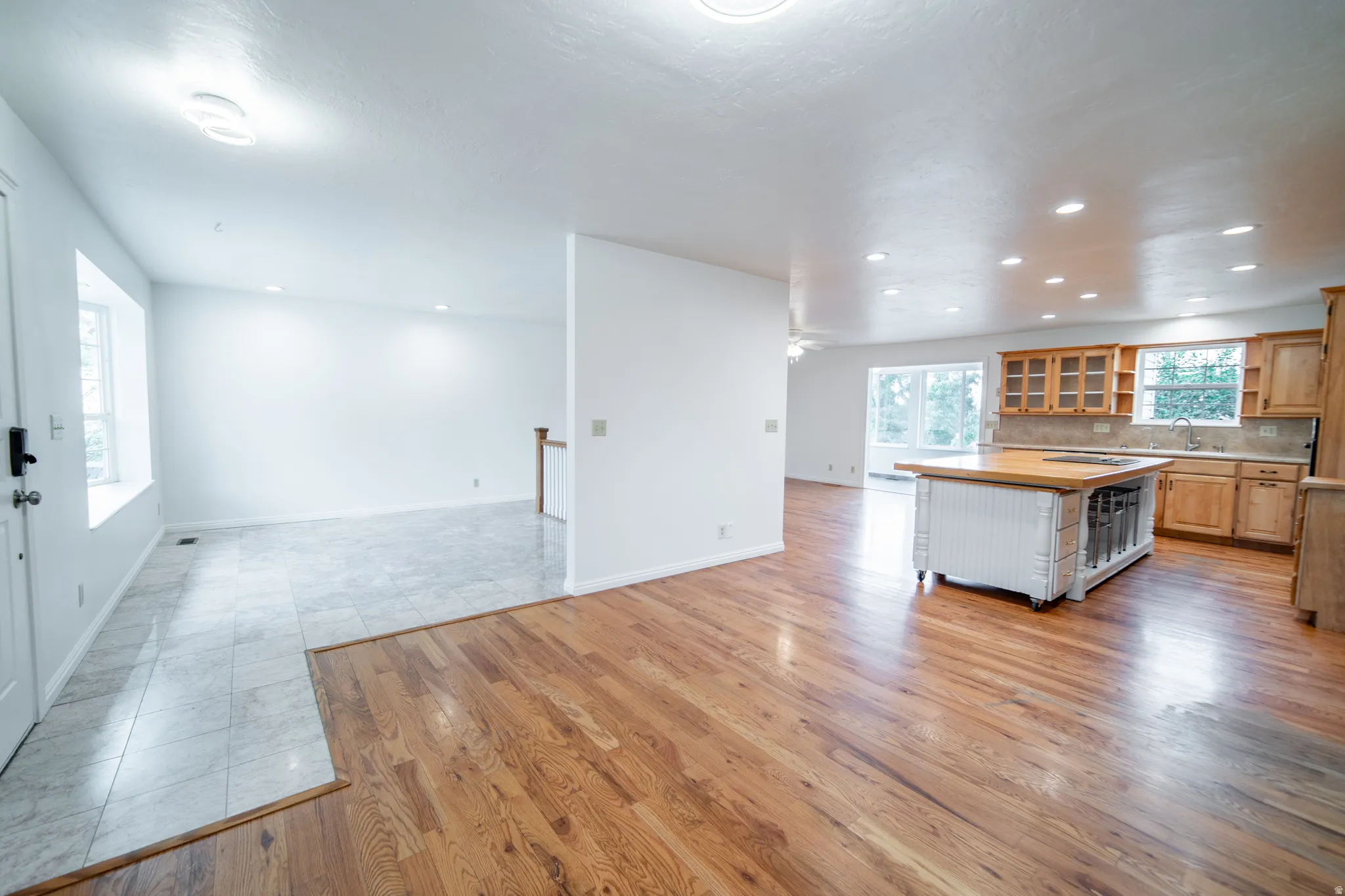 Hardwood flooring, recessed lighting, kitchen island with wood countertop, light wood cabinetry, and tiled flooring.
