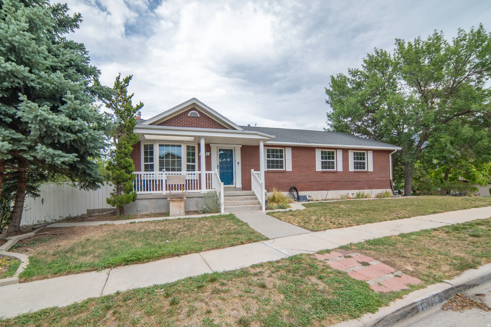 Brick exterior with white trim, front porch with white railings, and mature trees