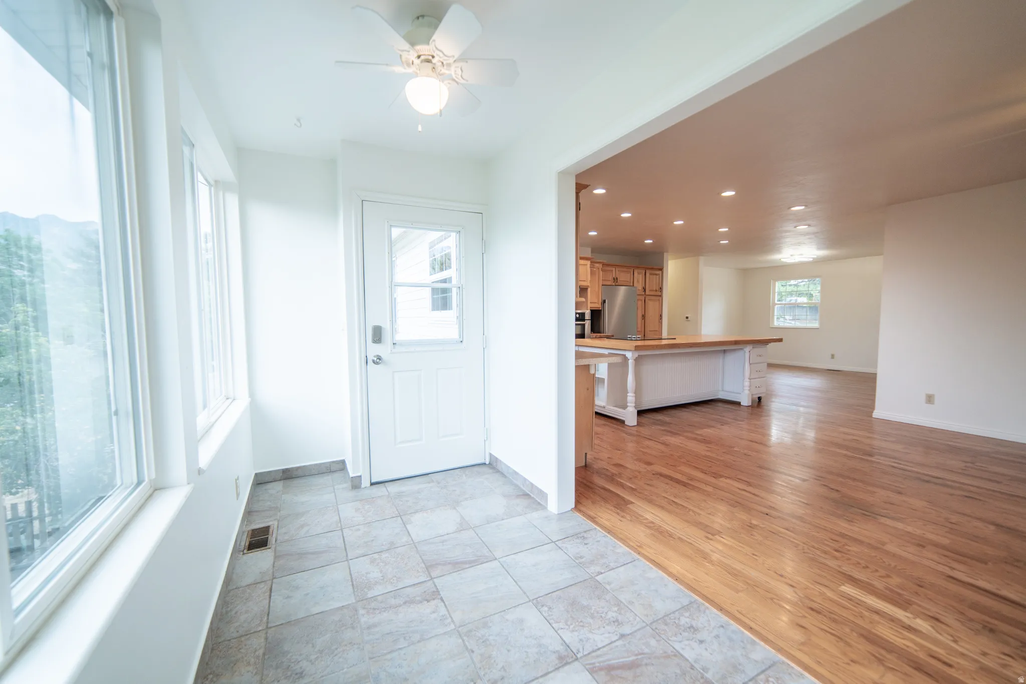 Entry with tile flooring, ceiling fan, opens to a wood-finish flooring, recessed lighting, kitchen.