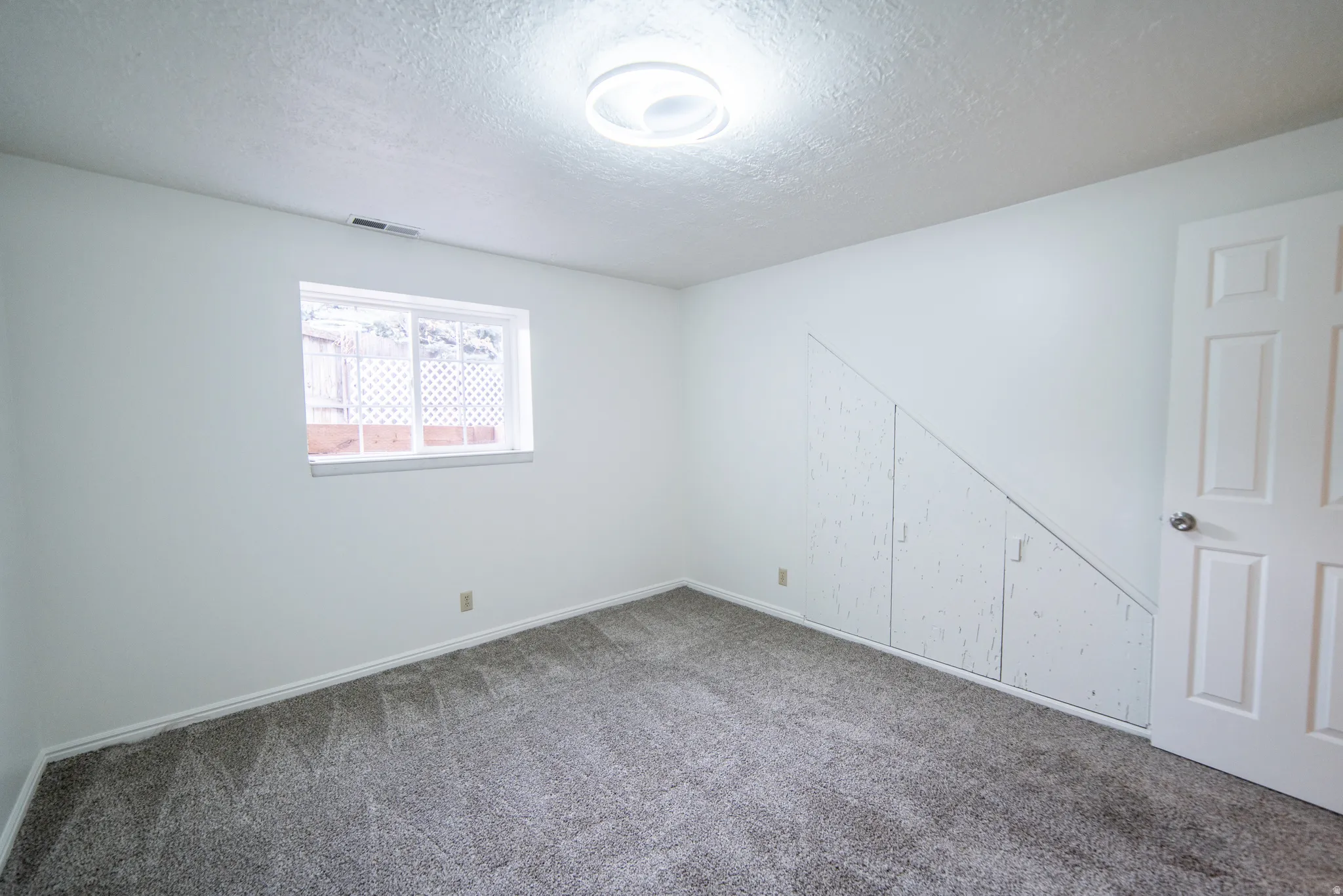 Spacious bedroom with neutral wall finishes, carpeted flooring, recessed ceiling lighting, and ample natural light from a window