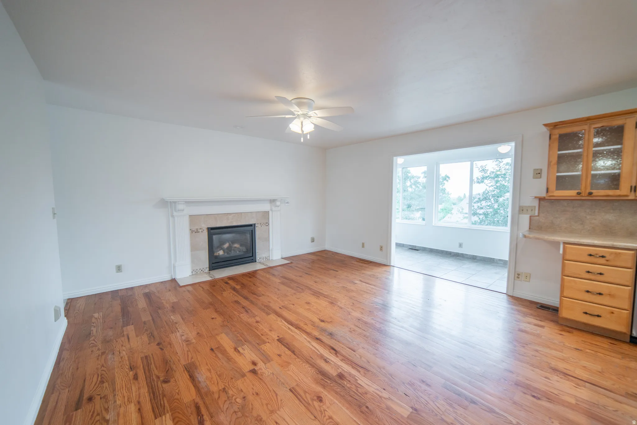 Hardwood flooring throughout, a gas fireplace with a decorative mantel, and a ceiling fan with integrated lighting.