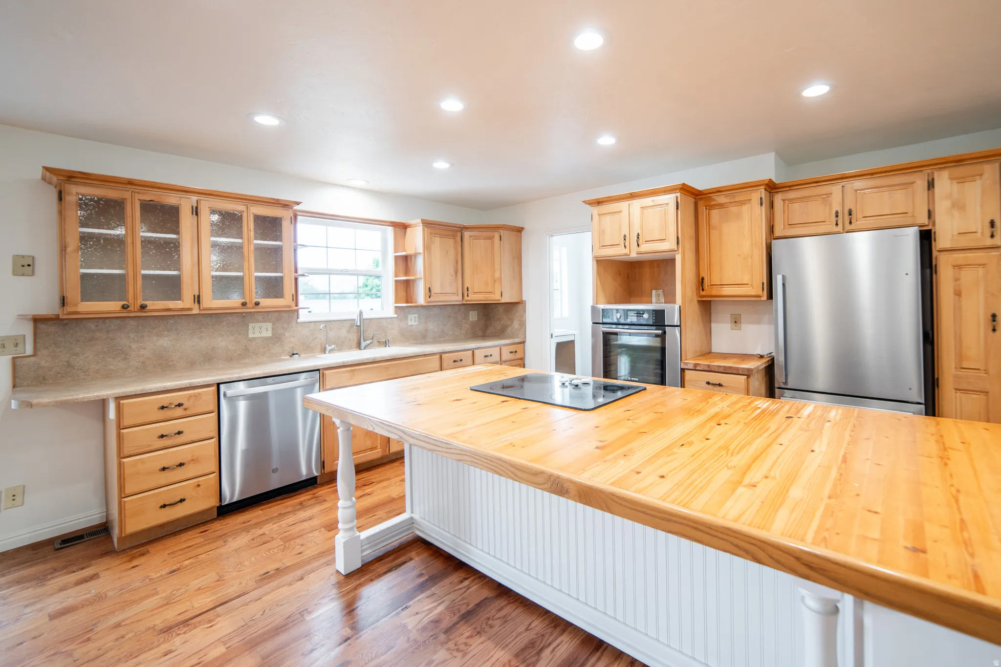 Kitchen featuring wood-finish flooring, recessed lighting, wood cabinetry, stone-finish countertops, and stainless steel appliances.