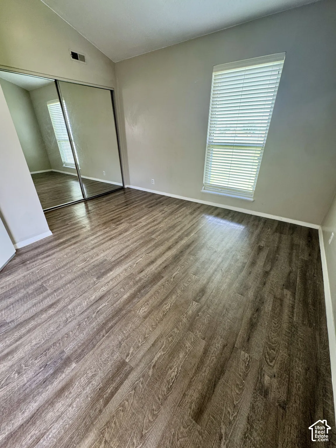 Wood-finish flooring, mirrored closet doors, vaulted ceiling, and a large window with blinds