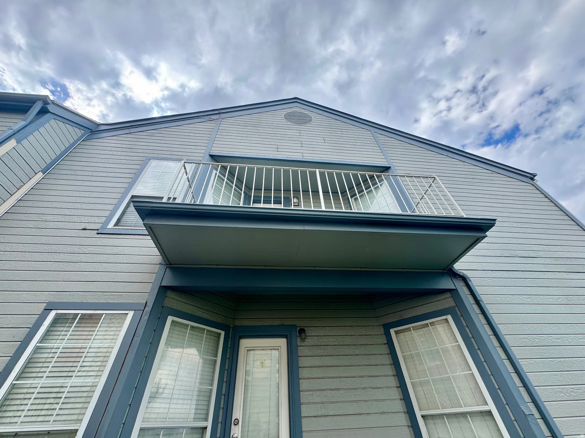 Exterior features horizontal siding, a private balcony with white railing, and multiple windows with white trim