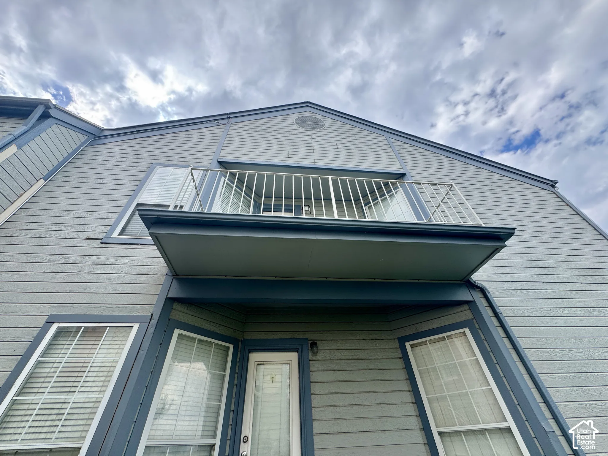 Exterior features horizontal siding, a private balcony with white railing, and multiple windows with white trim
