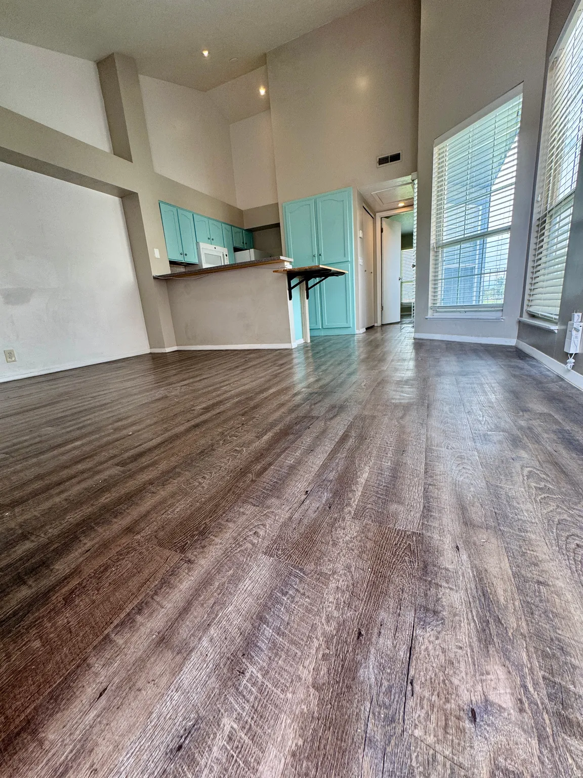 Vaulted ceilings with recessed lighting, wood-finish flooring, kitchen with teal cabinetry, breakfast bar, and white appliances