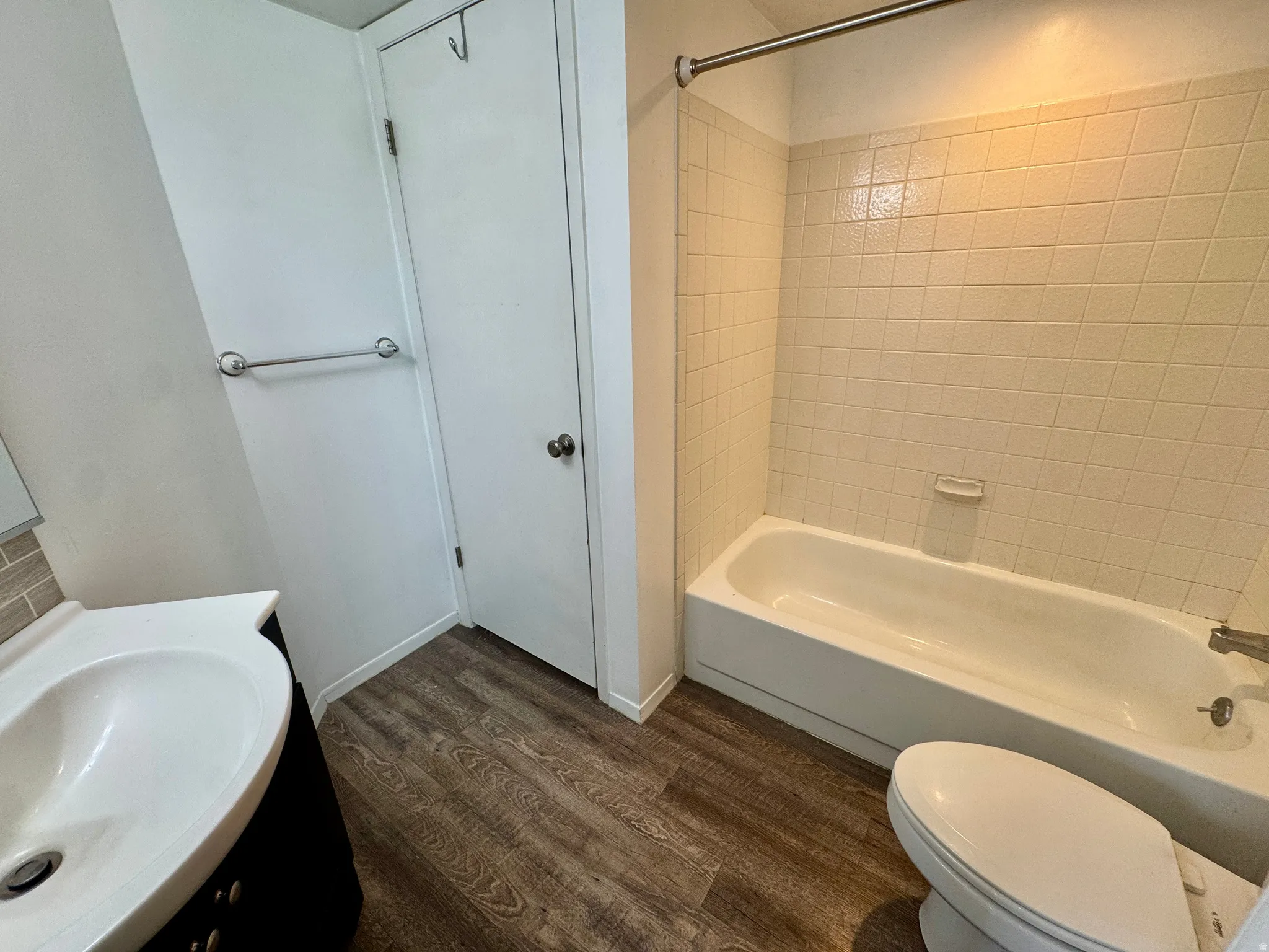 Wood-finish flooring with a white vanity featuring a sink, white toilet, and a bathtub with tiled surround