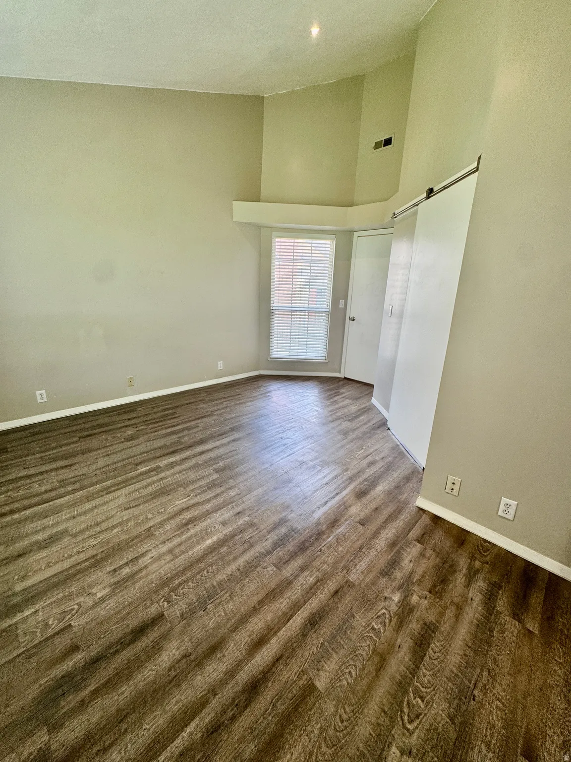 Vaulted ceiling with a wood-finish flooring, featuring a window with blinds and a sliding barn door