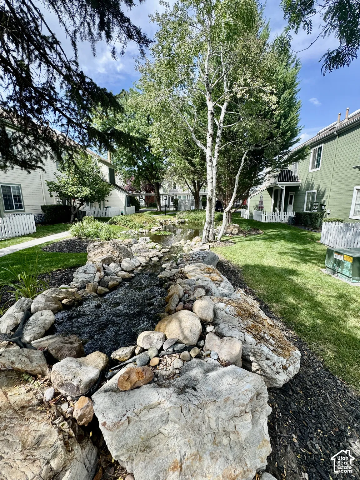 Landscaped water feature with natural rock elements, surrounded by a manicured lawn and mature trees