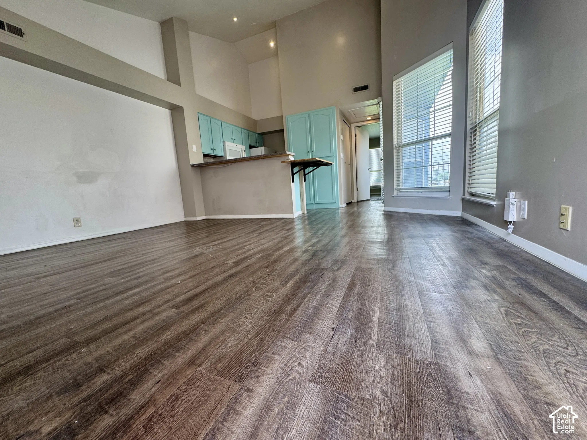 Vaulted ceilings, wood-finish flooring, kitchen with teal cabinetry, and large windows with blinds