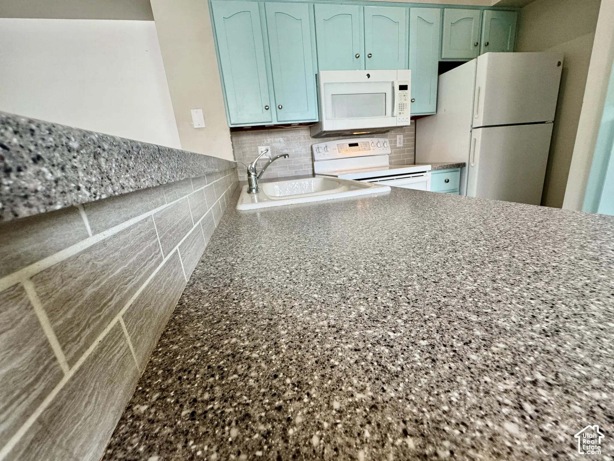Granite-look countertops, subway tile backsplash, white built-in microwave, white electric range, and white refrigerator