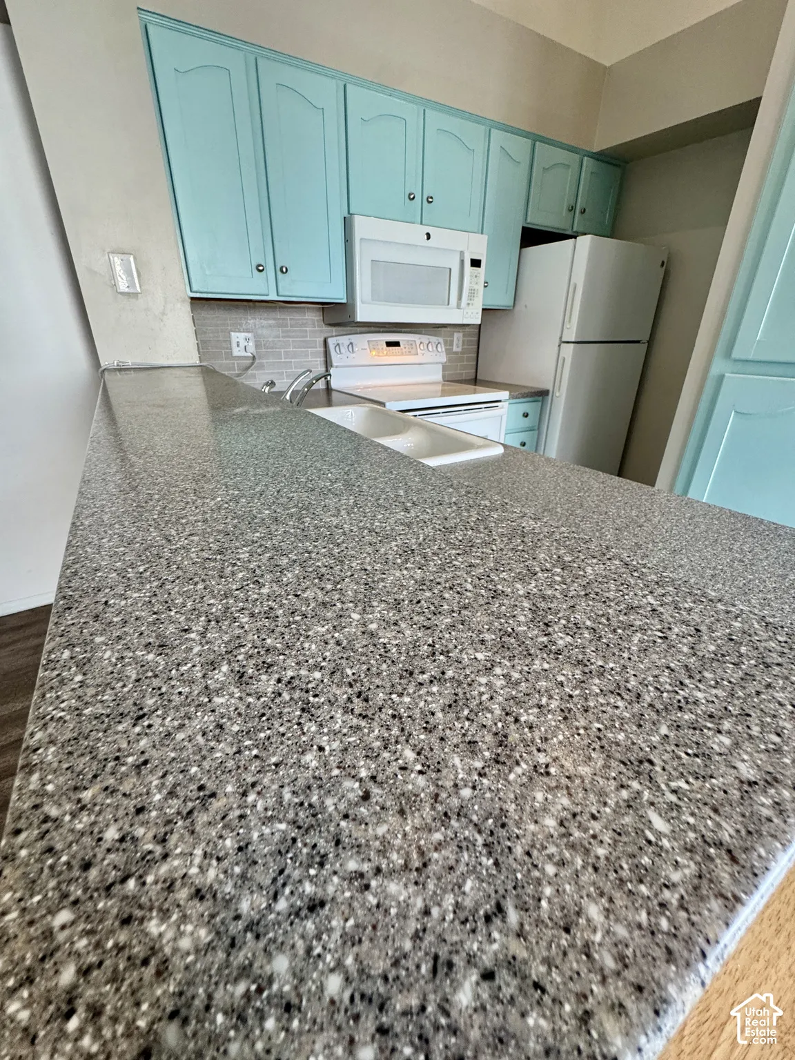 Granite-look countertop, integrated double basin sink, white built-in microwave, white electric range, and light blue cabinetry