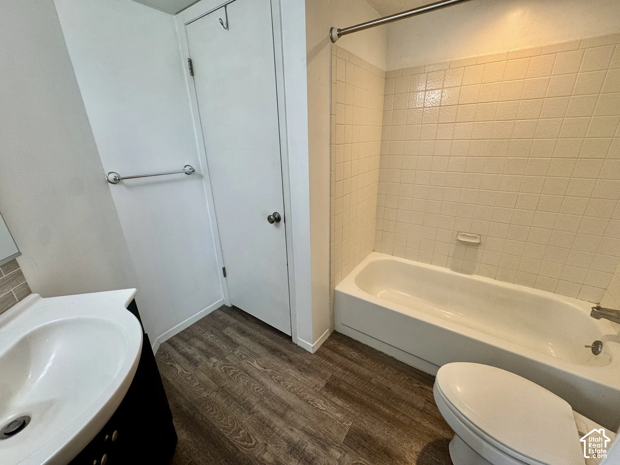 Wood-finish flooring with a white vanity featuring a sink, white toilet, and a bathtub with tiled surround