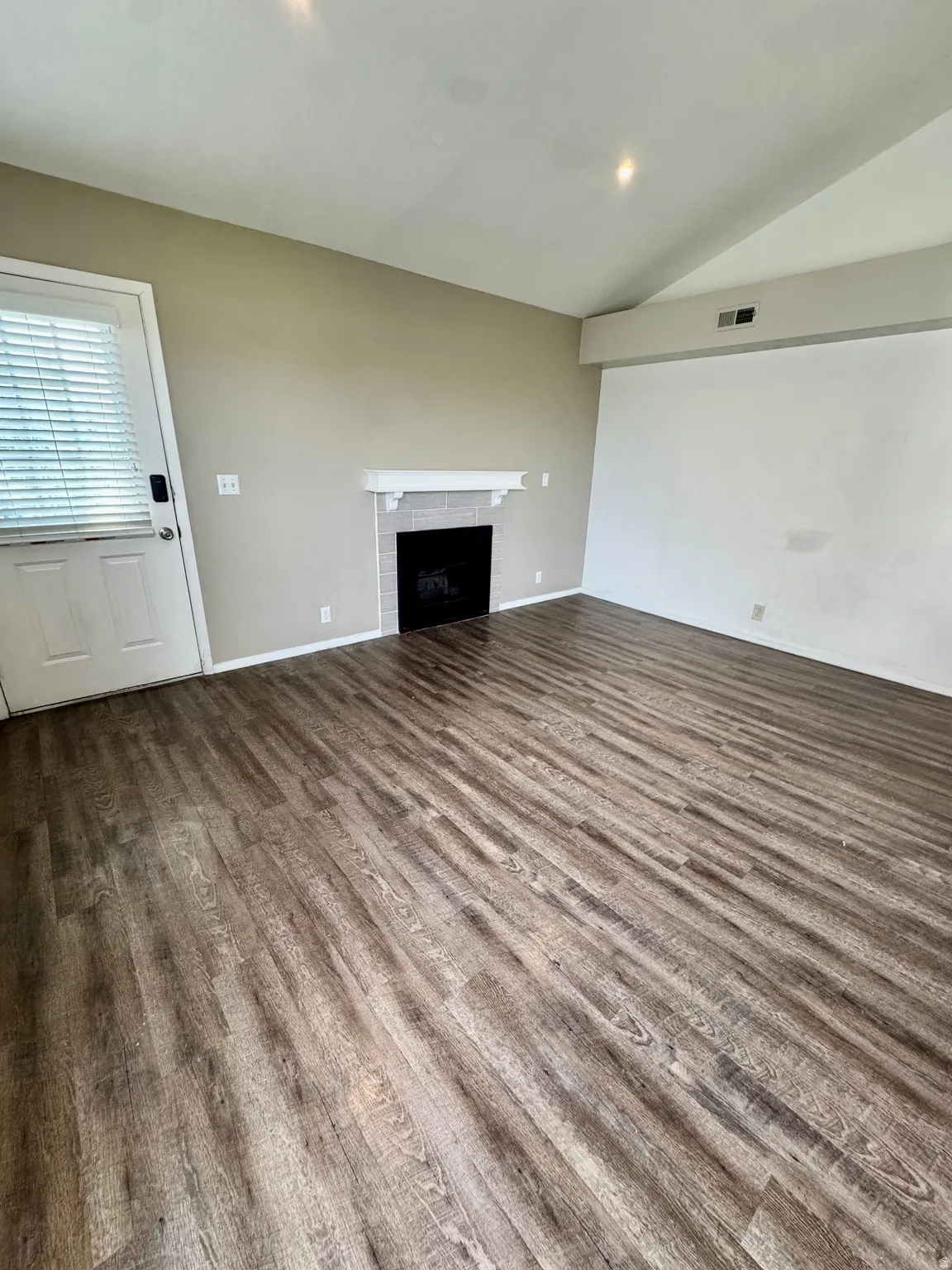 Wood-finish flooring, fireplace with tile surround and mantel, vaulted ceiling, and recessed lighting