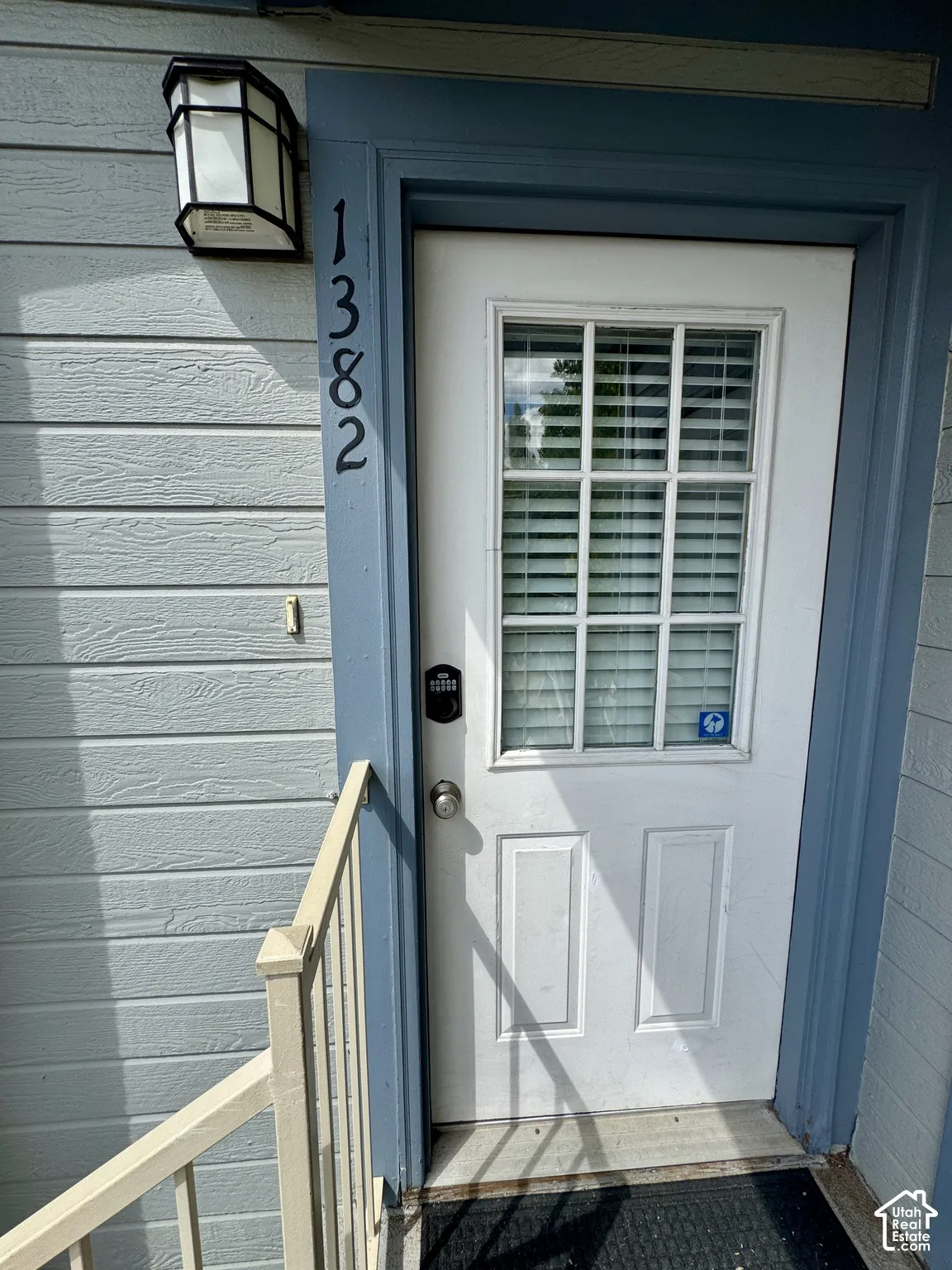 Entry door with upper window panes, digital keypad lock, and exterior light fixture
