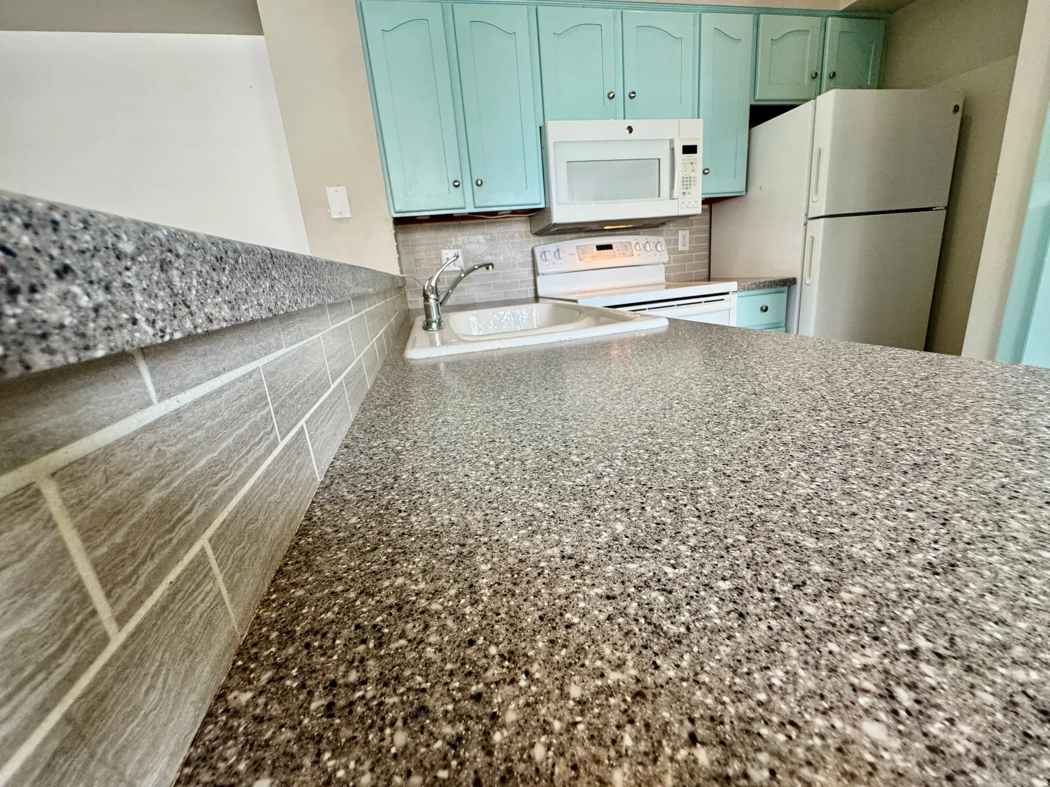 Granite-look countertops, subway tile backsplash, white built-in microwave, white electric range, and white refrigerator