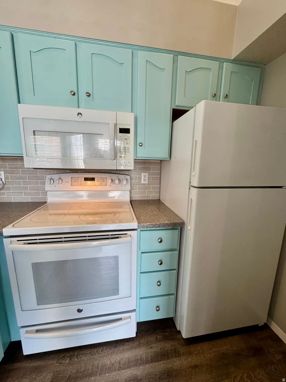 Kitchen featuring light teal cabinetry, white appliances, gray tile backsplash, and wood-finish flooring
